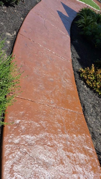 A red stamped concrete pathway in a backyard 